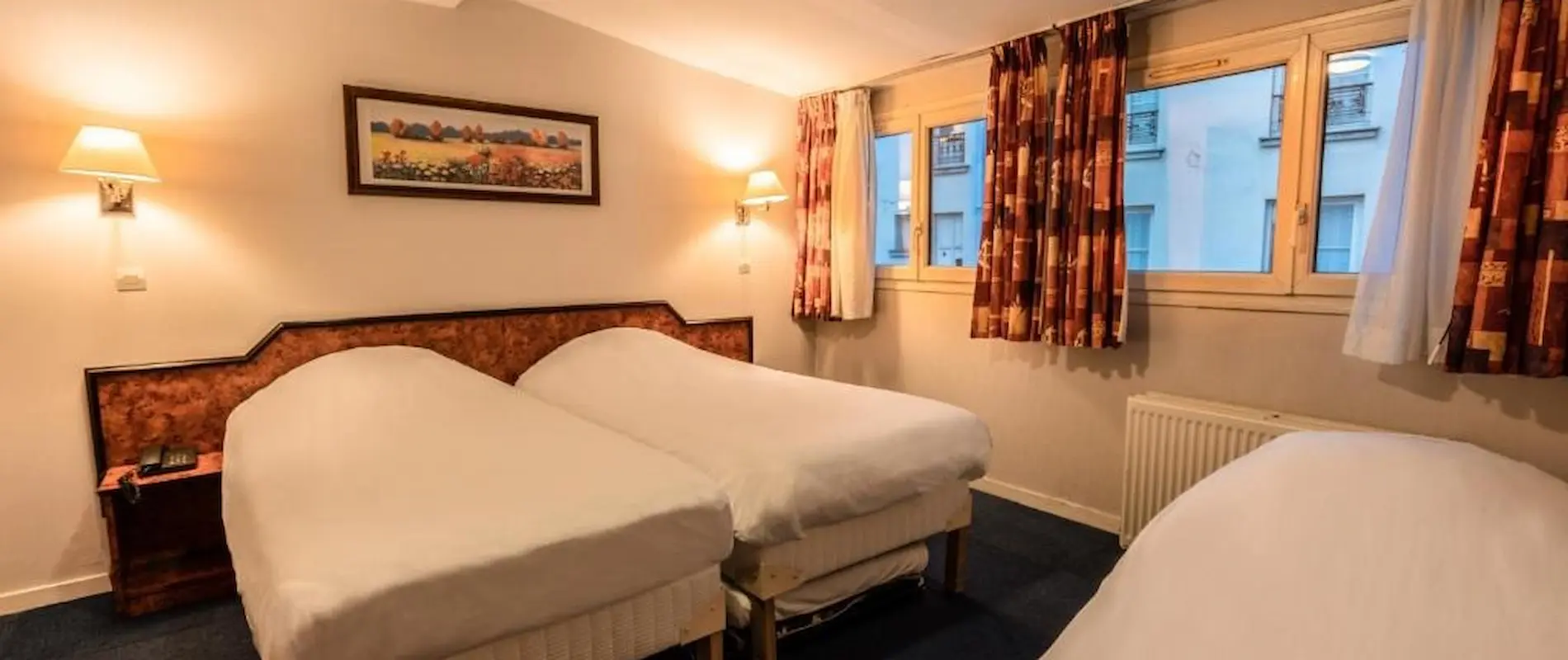 Chambre avec trois lits simples, deux lampes murales et un cadre au mur. Fenêtres avec rideaux.