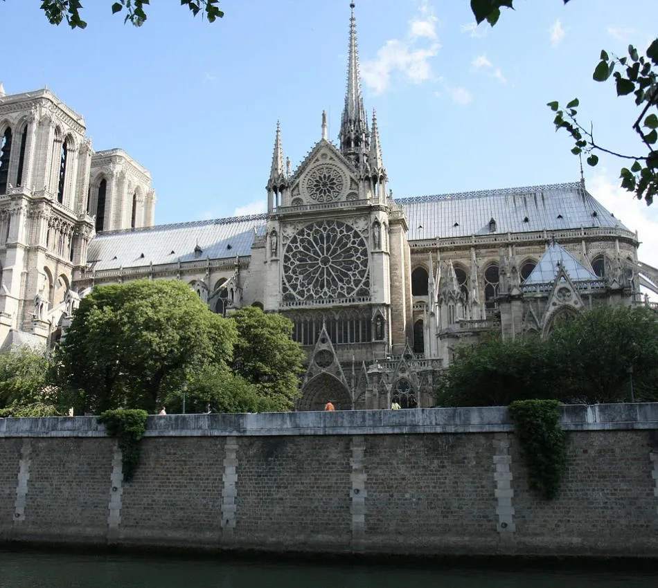 Cathédrale gothique avec rosace, entourée d'arbres et d'un mur en pierre.