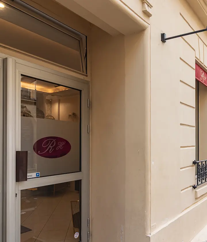 Entrée d'un bâtiment beige avec une porte vitrée et un logo rose.
