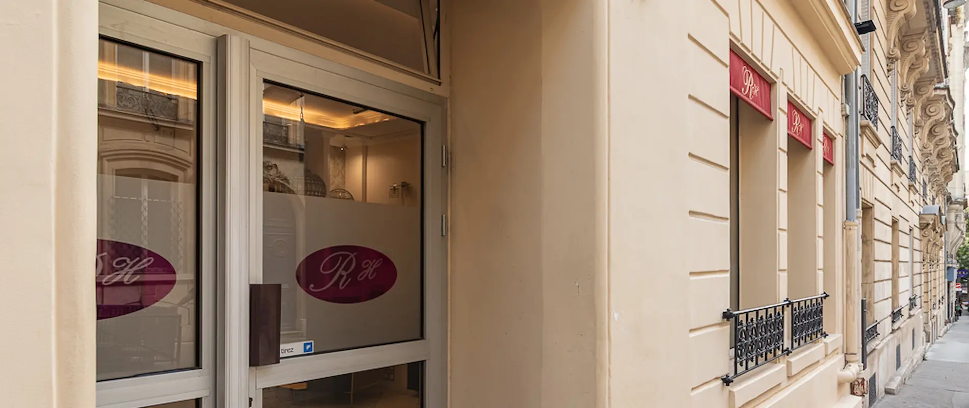 Entrée d’un bâtiment beige avec des fenêtres décorées de marquises rouges.