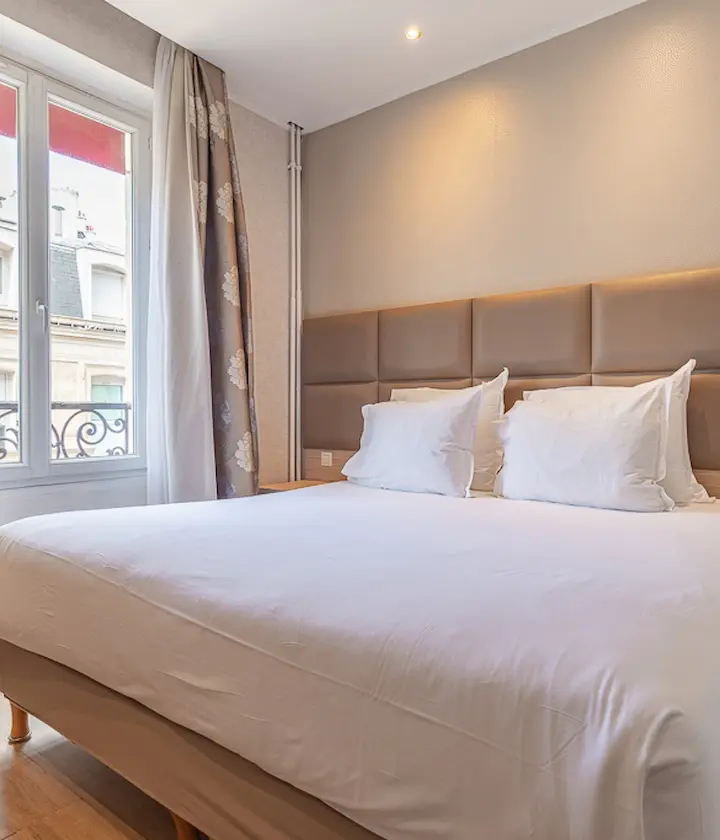 Chambre d'hôtel lumineuse avec lit double et fenêtre.