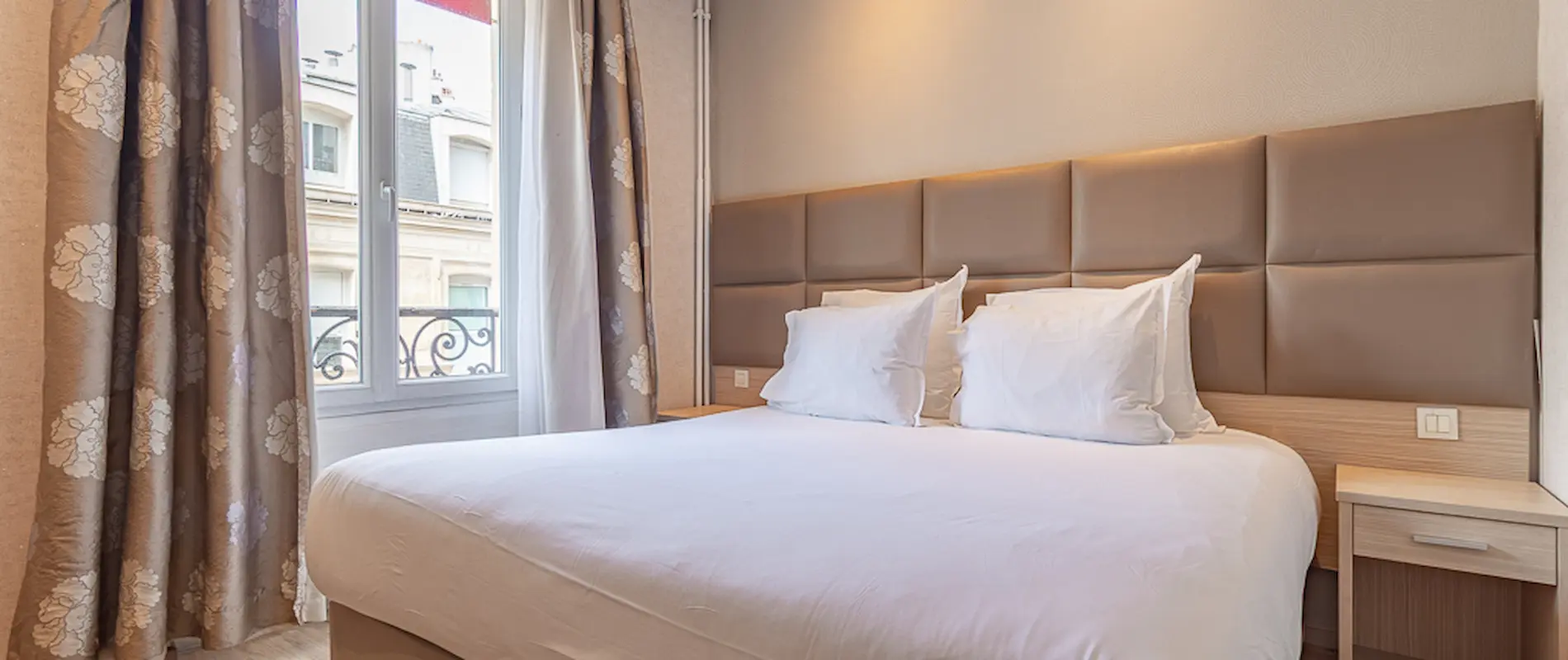 Lit double confort près d'une fenêtre avec rideaux fleurés.