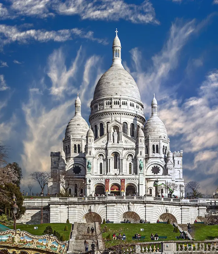 Basilique blanche sous un ciel bleu avec des nuages et des visiteurs sur la pelouse.