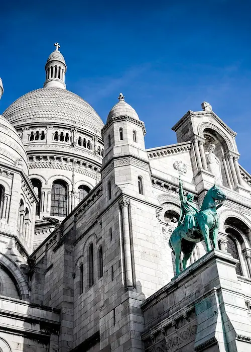 Basilique blanche avec dôme et statue équestre sous un ciel bleu.