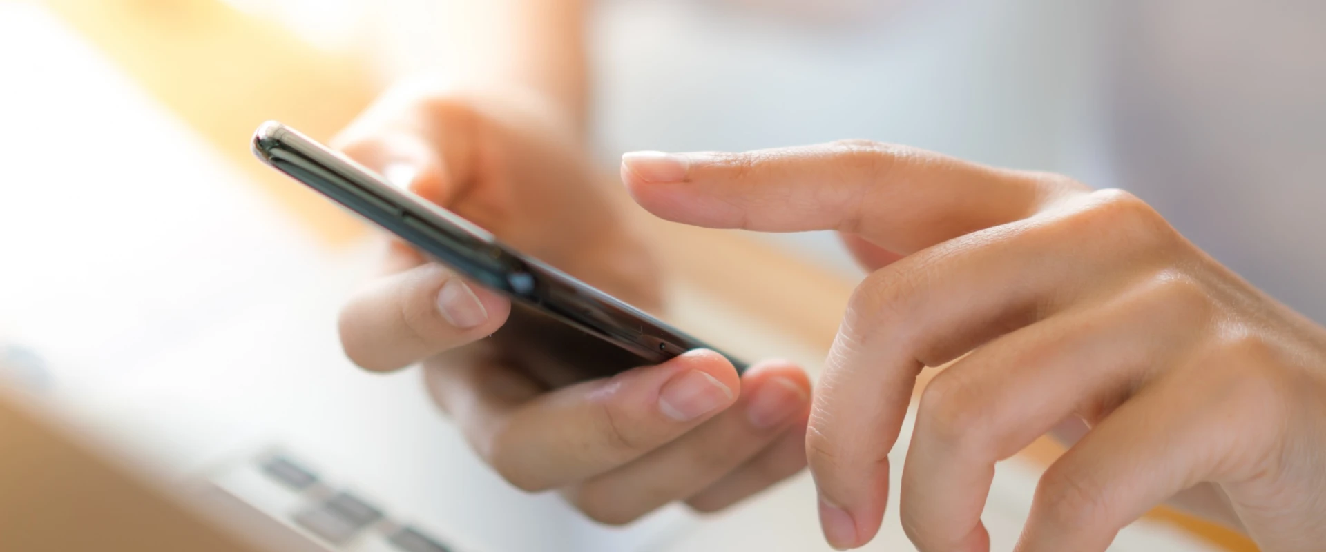 Personne utilisant un smartphone, clavier flou d'ordinateur en arrière-plan.