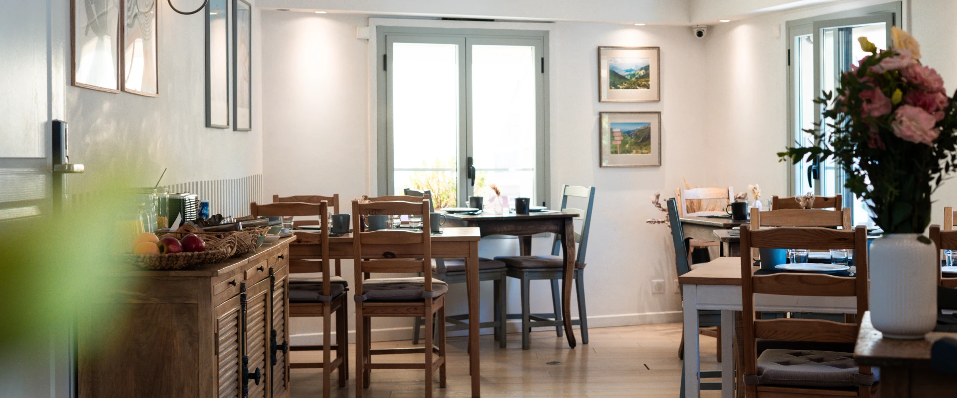 Salle à manger calme avec tables en bois, fleurs et lumière naturelle.