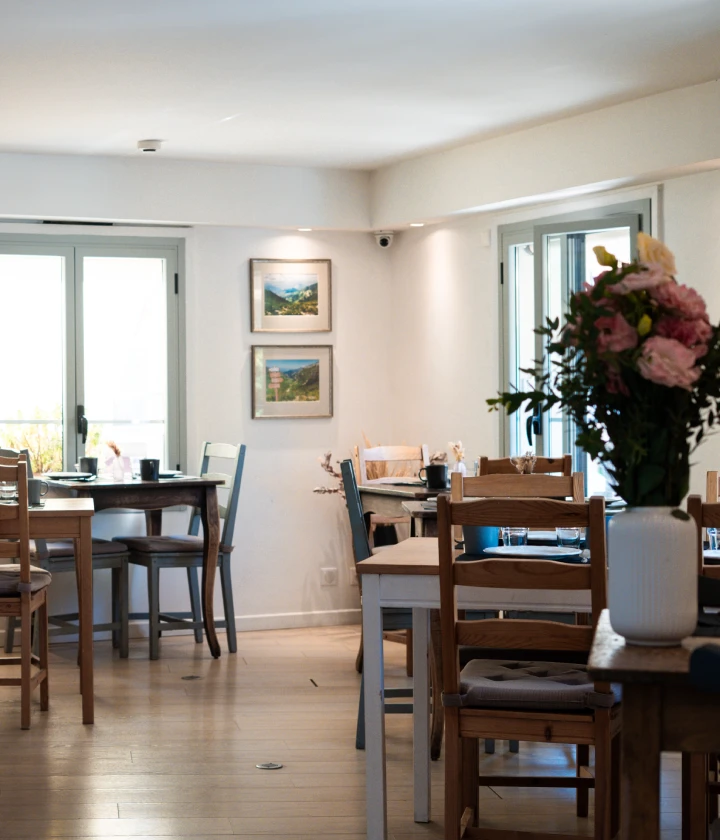 Salle à manger lumineuse avec tables en bois, fleurs, et tableaux sur le mur.