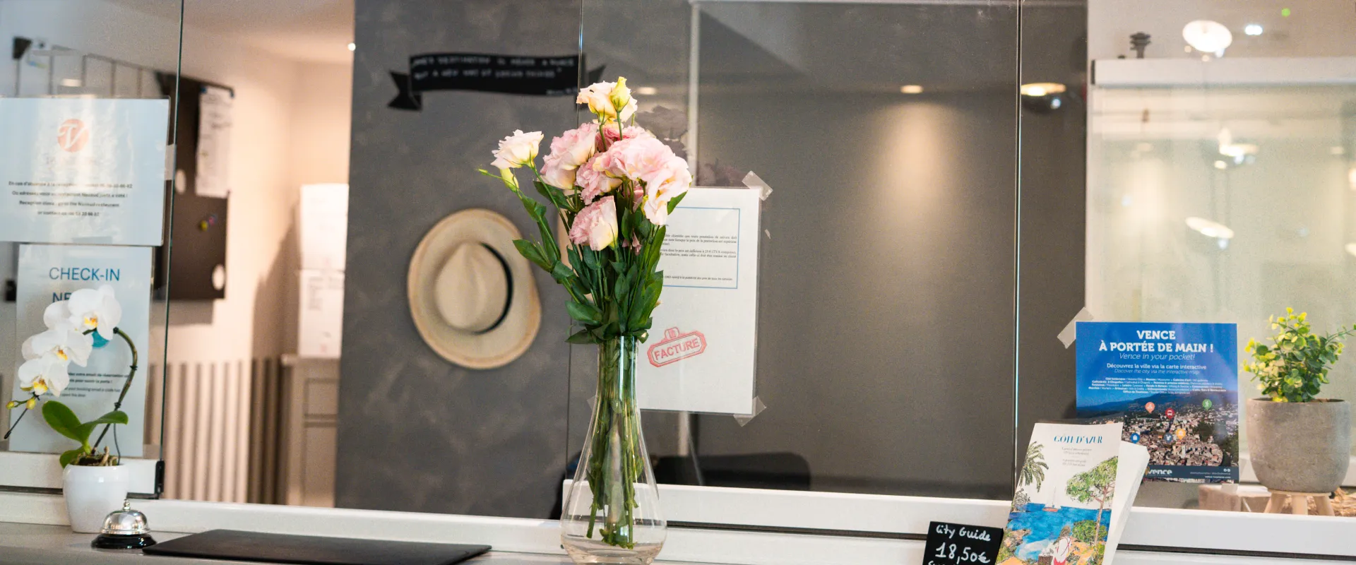 Vase de fleurs roses sur un comptoir, affiches et chapeau suspendu en arrière-plan.