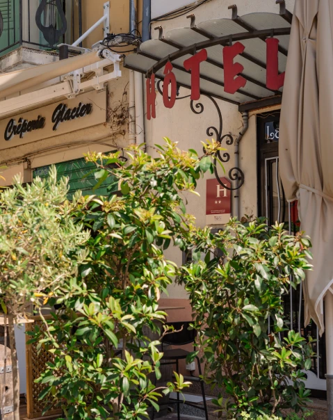Façade d'un hôtel et d'une crêperie, avec des plantes en premier plan.