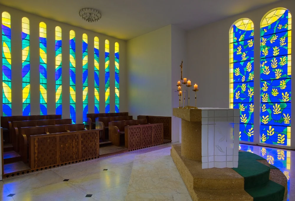 Chapelle avec vitraux colorés, bougies allumées sur l'autel et rangées de bancs.