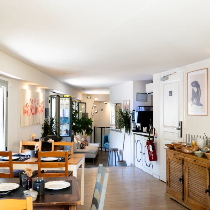 Salle à manger lumineuse avec mobiliers en bois, œuvres murales, plantes et coin salon.