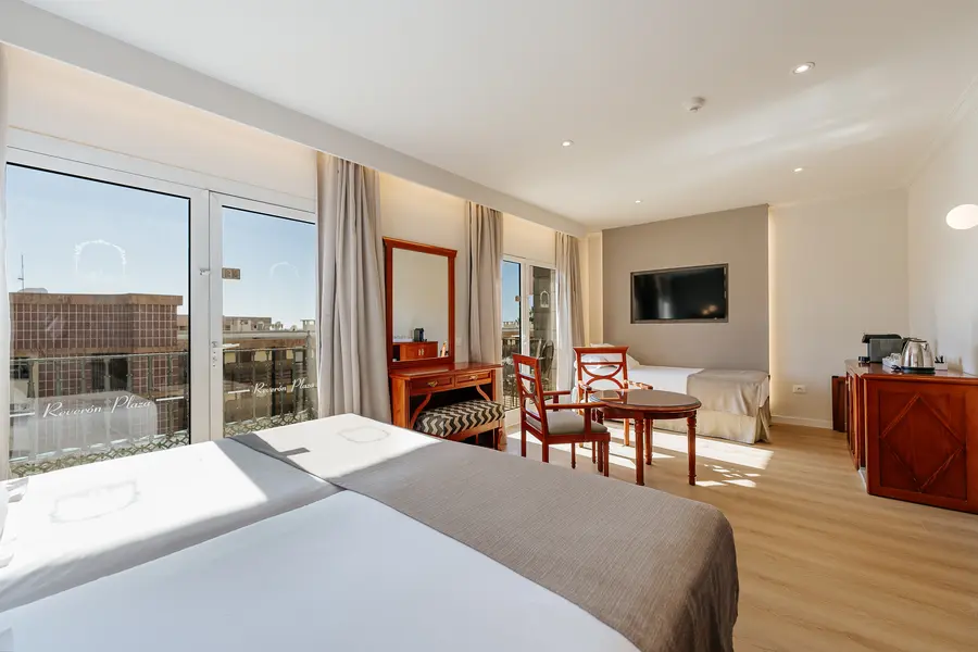 Habitación luminosa con cama doble, televisor y muebles de madera.