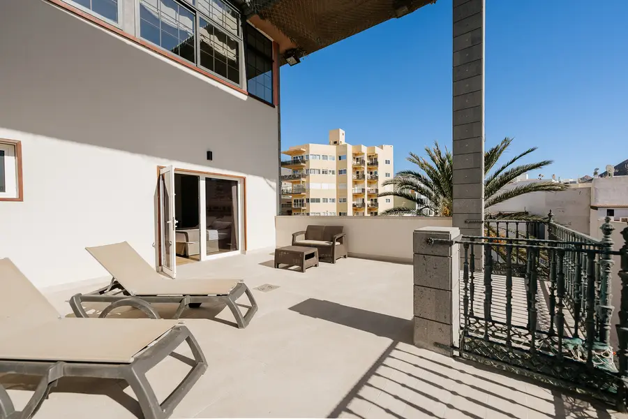 Terraza soleada con tumbonas y muebles de exterior, edificios al fondo.