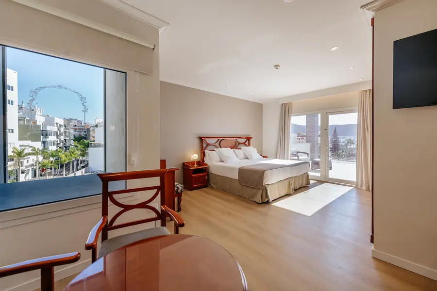 Habitación amplia con cama doble, muebles elegantes y ventana con vista a la ciudad.