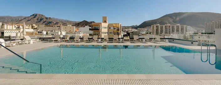 Piscina en la azotea con vista a la ciudad y montañas al fondo.