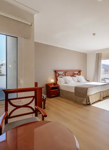 Habitación de hotel con cama doble, decoración en madera y ventana al fondo.