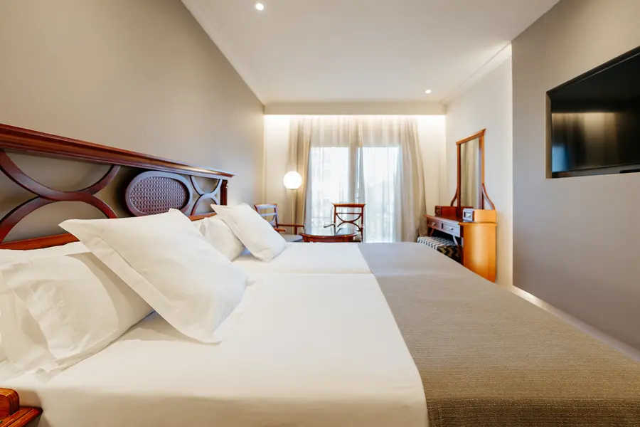 Habitación de hotel moderna con dos camas, TV y ventana luminosa.