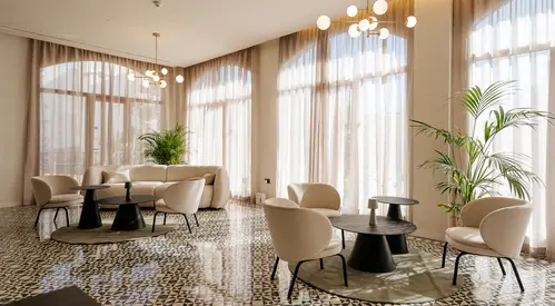 Sala moderna con muebles claros y plantas, iluminación suave y cortinas largas.