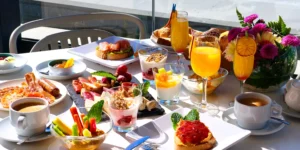 Mesa de brunch al aire libre con zumos de naranja, tostadas con salmón, yogur con frutas y embutidos.