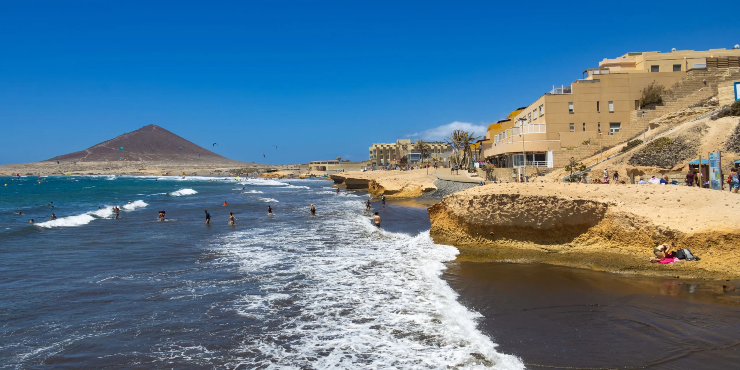 Playa de El Médano con bañistas en la orilla del mar y la Montaña Roja al fondo en el sur de Tenerife.