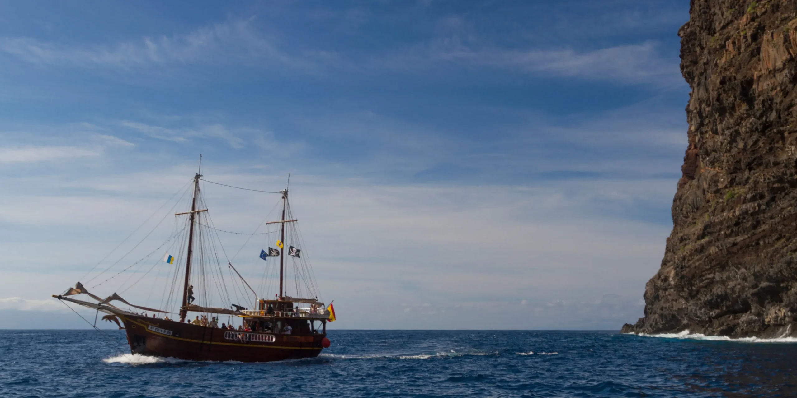Barco pirata de excursión navegando por el mar azul junto a los acantilados de Los Gigantes en Tenerife.