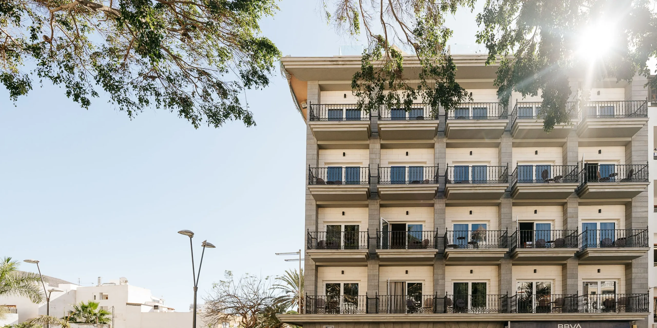 Fachada moderna de un edificio del hotel Reverón Plaza con balcones de forja bajo la luz del sol en Los Cristianos.