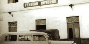 Fotografía histórica en sepia de la fachada de la antigua Pensión Reverón en Los Cristianos, Tenerife, con un vehículo de la época estacionado enfrente.