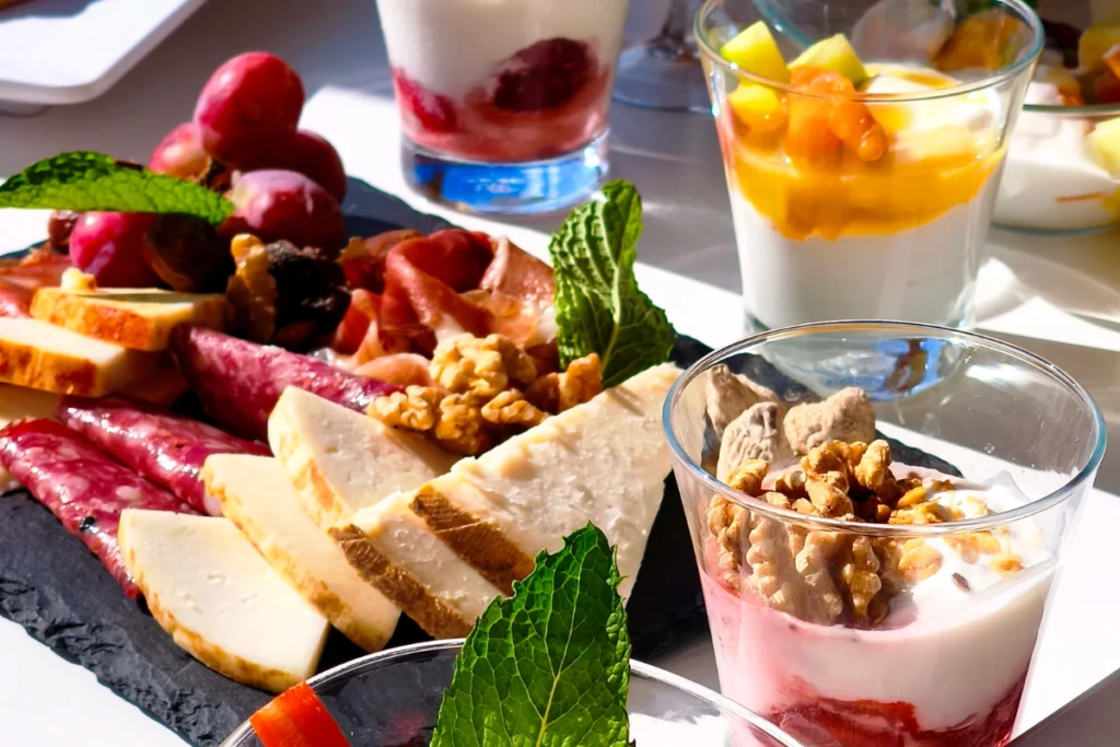 Primer plano de tabla de embutidos, quesos, nueces y vasos de yogur con frutas del brunch en Amanay Sky Bar.