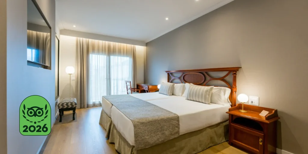 Habitación doble del Hotel Reverón Plaza en Los Cristianos, Tenerife, con un logotipo superpuesto que indica el premio Travelers' Choice de TripAdvisor de 2026.