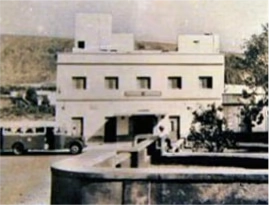 foto antigua con edificio antiguo con veh&iacute;culo cl&aacute;sico estacionado al frente.