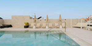 Zona de piscina y solárium en la azotea del Hotel Reverón Plaza en Los Cristianos, Arona, con tumbonas alineadas frente a la barandilla de acceso al agua.