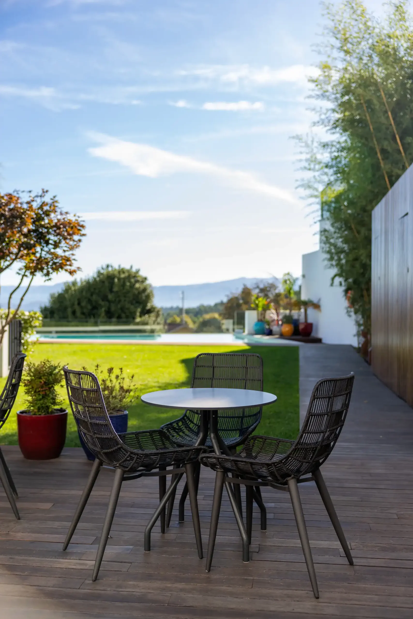 Mesa ao ar livre com cadeiras em deck, cercada por jardim e plantas.