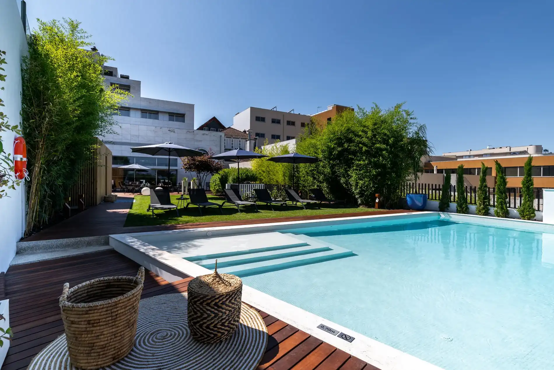 Piscina com espregui&ccedil;adeiras e guarda-s&oacute;is em um terra&ccedil;o ensolarado.