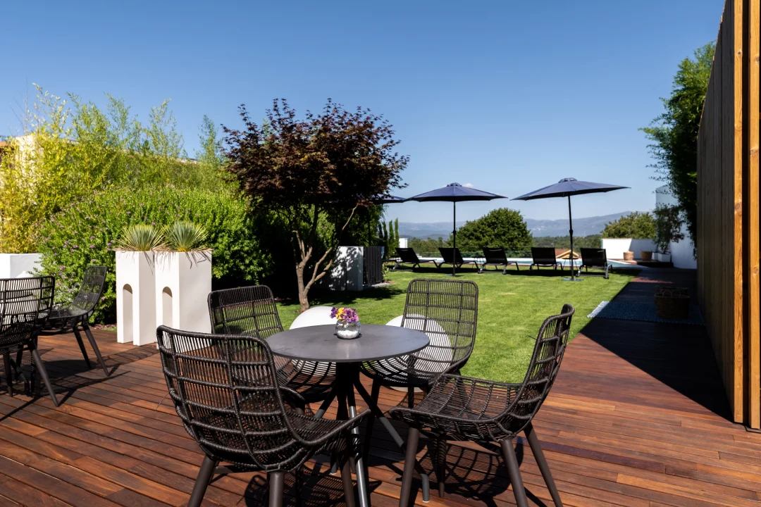 Terra&ccedil;o com mesa, cadeiras e jardins sob c&eacute;u azul claro.