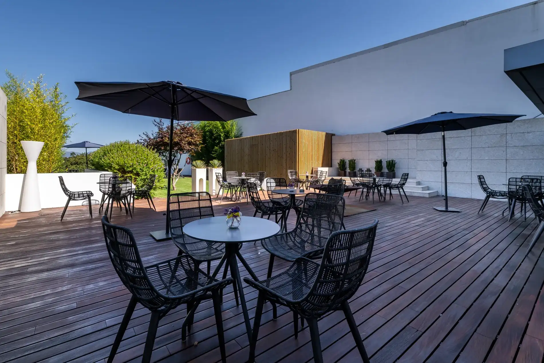 &Aacute;rea externa com mesas, cadeiras e guarda-s&oacute;is em piso de madeira.