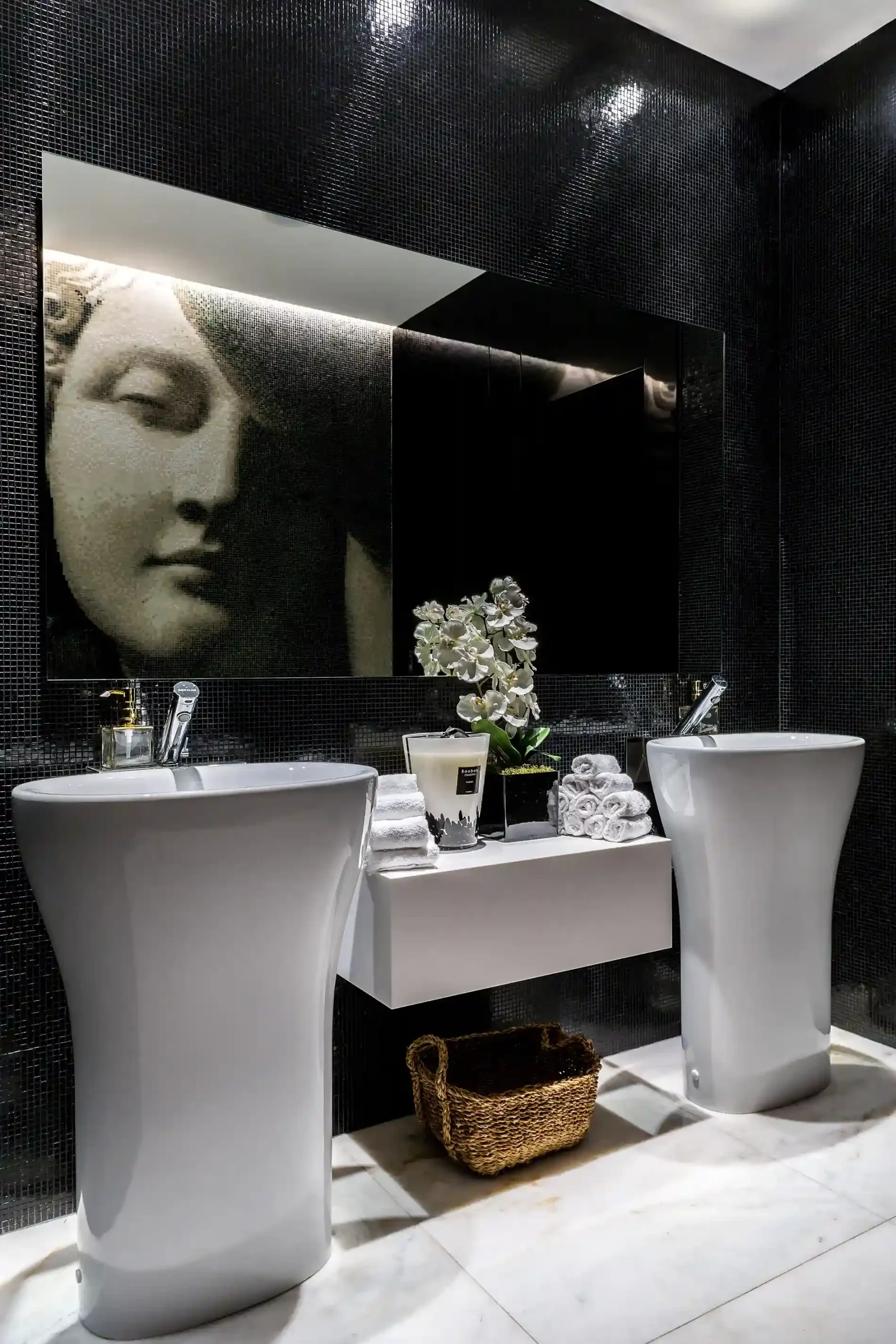 Banheiro elegante com dois lavat&oacute;rios, arte de rosto e decora&ccedil;&atilde;o floral.