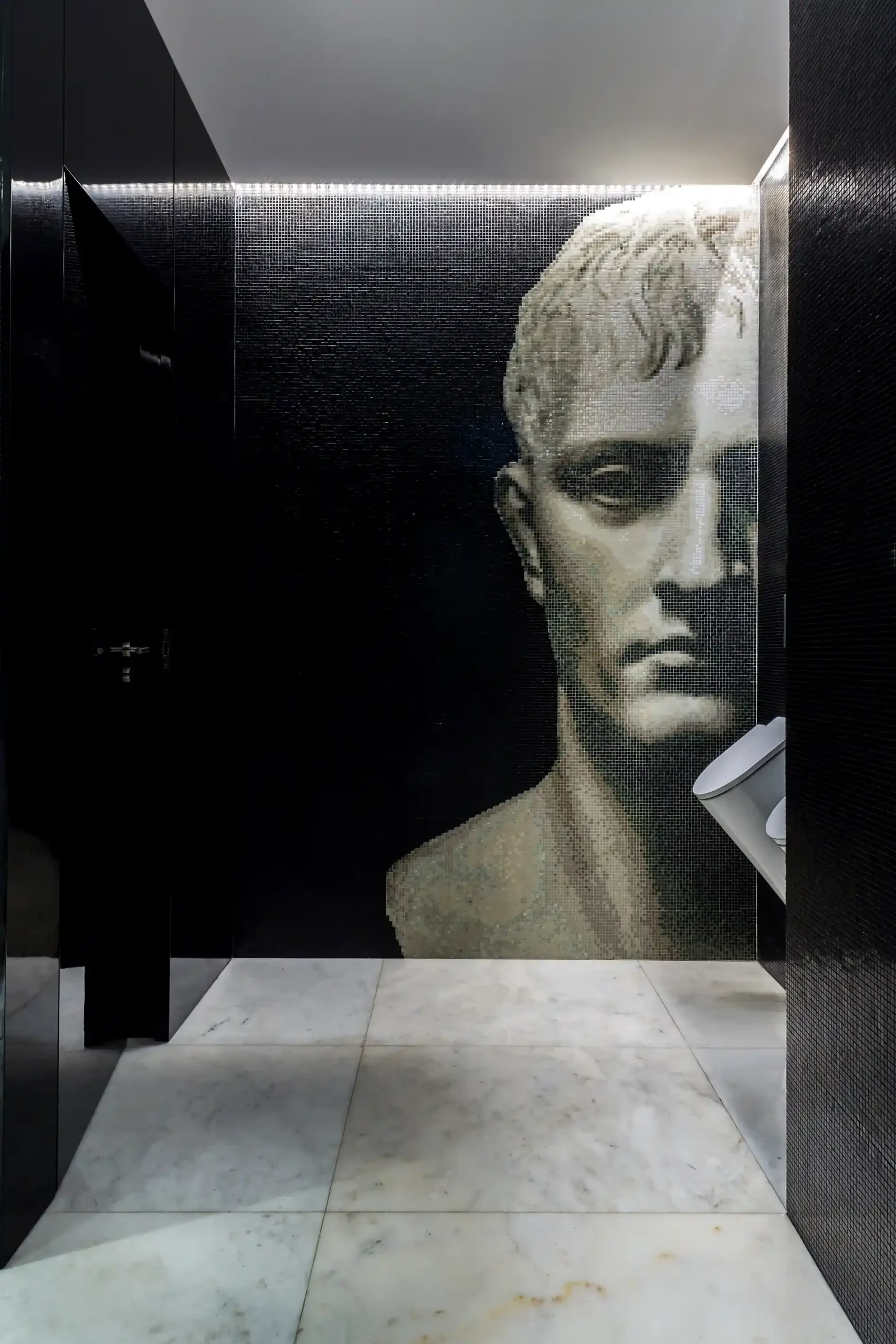 C&acirc;mara escura com mosaico de rosto esculpido em parede de azulejos pretos.