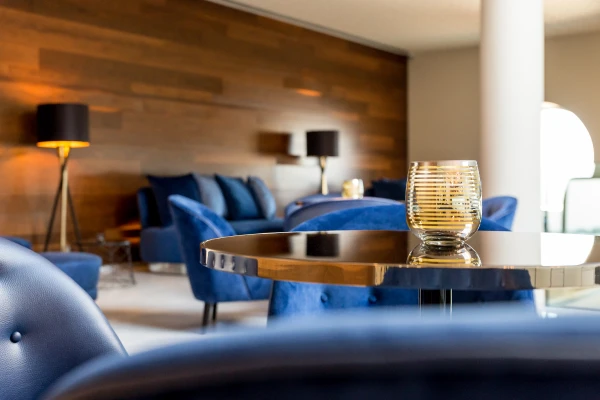 Sal&atilde;o de lounge elegante com poltronas azuis e mesa com vela decorativa.