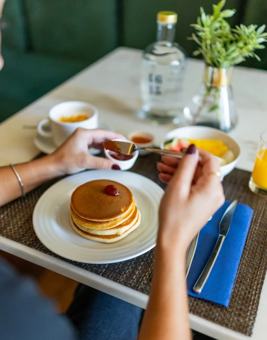 Pessoa colocando geleia em panquecas em mesa de caf&eacute; da manh&atilde;.