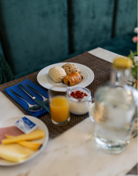 Caf&eacute; da manh&atilde; com p&atilde;es, iogurte, suco e frios sobre a mesa.