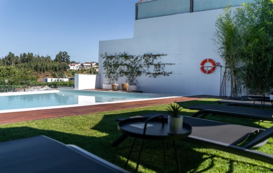 Piscina moderna com espregui&ccedil;adeiras e ampla &aacute;rea verde ao redor.