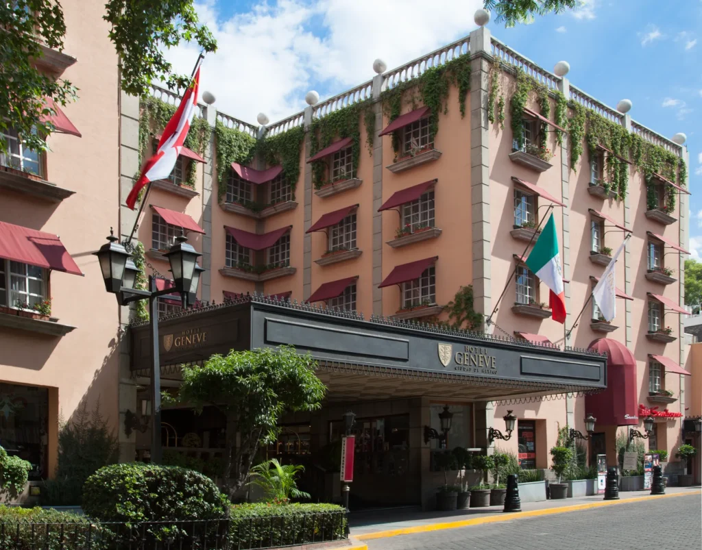 Fachada del Hotel Geneve con banderas en la entrada, ventanas con toldos rojos y plantas decorativas.