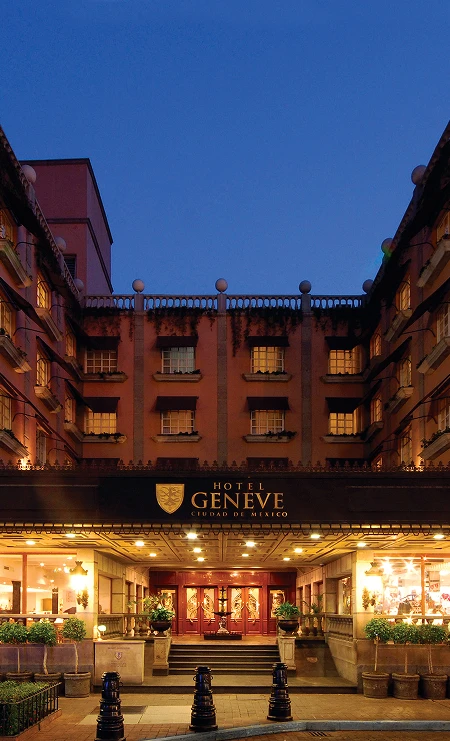Fachada iluminada del Hotel Geneve en la Ciudad de M&eacute;xico al anochecer, con entrada principal y ventanas visibles.