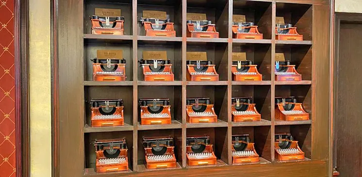 Estanter&iacute;a con varias m&aacute;quinas de escribir antiguas naranjas, distribuidas en filas de cinco.