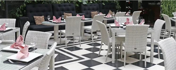 Restaurante elegante con sillas blancas y mesas con servilletas rosadas sobre suelo ajedrezado en blanco y negro.