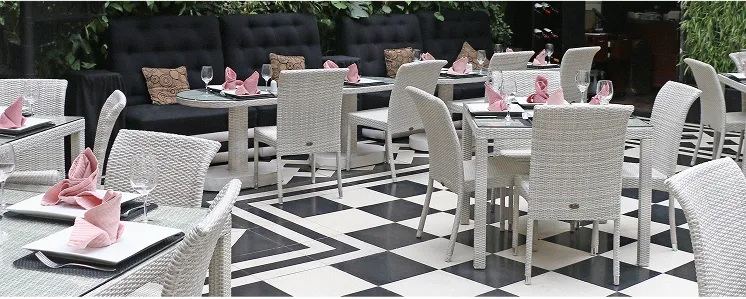 Restaurante elegante con sillas blancas y mesas con servilletas rosadas sobre suelo ajedrezado en blanco y negro.