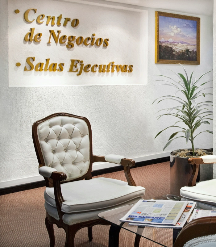 &Aacute;rea de oficina ejecutiva con silla cl&aacute;sica tapizada, mesa auxiliar y plantas decorativas.