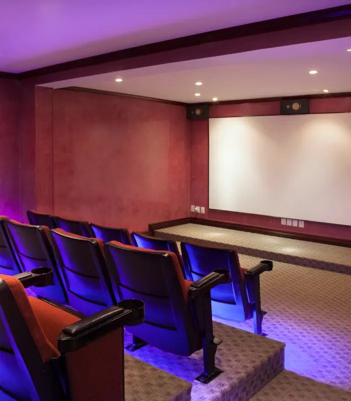 Home theater room with red walls, tiered seating, blue accent lights, and a large screen at the front.