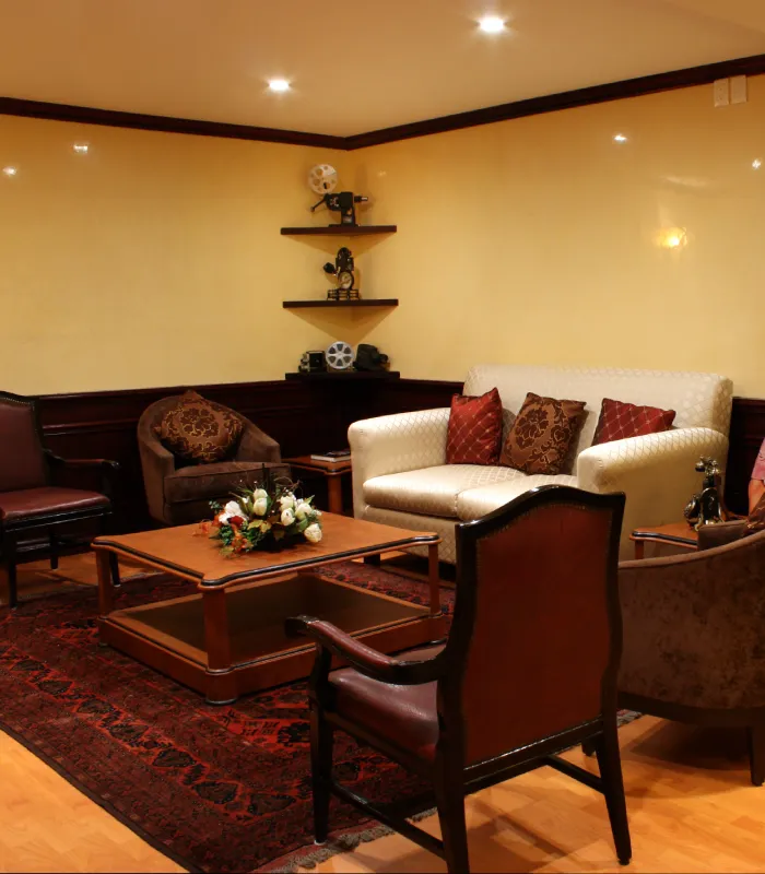 Cozy living room with sofas, a coffee table, and decorative items on shelves. Warm lighting and floral centerpiece.