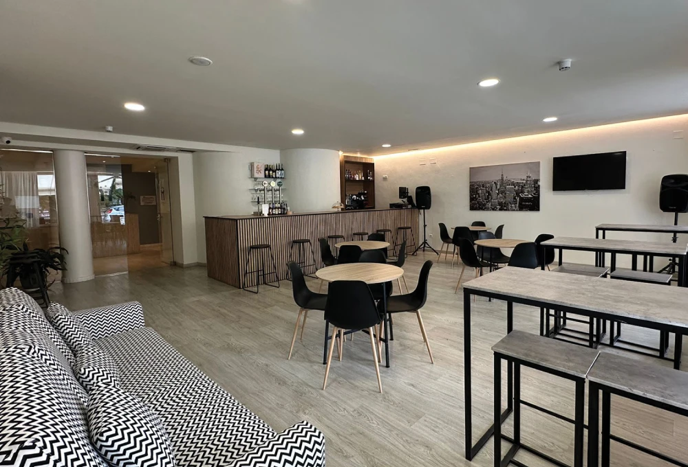 Sala moderna con mesas, sillas, barra de bar, sofá y decoración en tonos neutros.